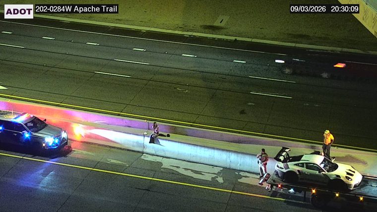 Police car with blue and red lights on the shoulder, and a tow truck with a sports car on it