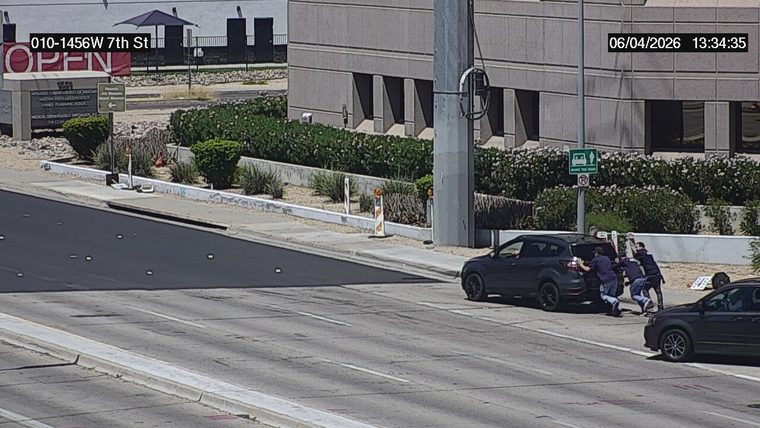 Three people pushing a dark colored SUV off the travel lane