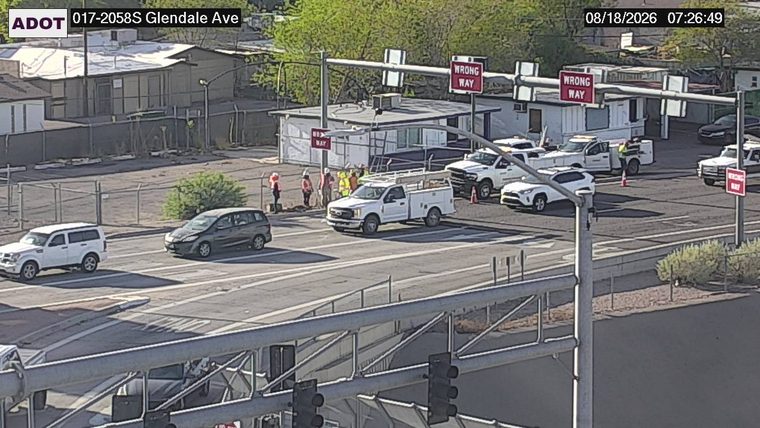 Several workers in high-visibility vests gathered near a white truck, with orange traffic cones present.