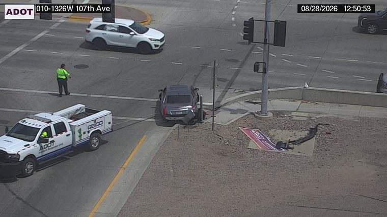 Gray sedan with visible damage to the rear bumper and trunk, partially on the sidewalk