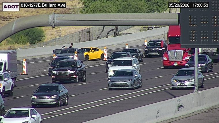 Multiple vehicles stopped on the left shoulder with people standing outside and traffic cones set up
