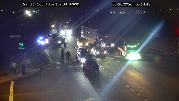 Two police cars with blue lights activated and several individuals standing in the roadway