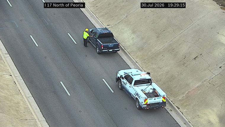 ADOT Incident Response Unit vehicle with lights on and a person in hi-viz vest near a pickup truck on the right shoulder