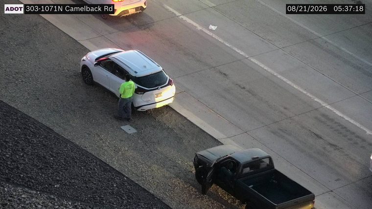 Person in high-visibility vest standing next to a white SUV on the shoulder