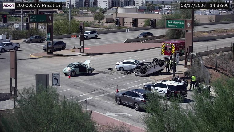 A white car overturned in the intersection with debris on the roadway, a police car, and an ambulance present