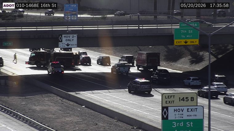 Multiple emergency responder vehicles, including fire engines and police cars with flashing lights, blocking the left lanes under the overpass, with a responder on foot on the left shoulder