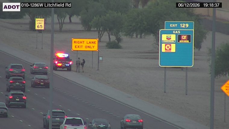 Police car with lights on the shoulder and two individuals standing nearby