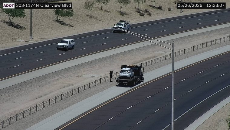 Tow truck carrying a white car on the left shoulder with a person standing nearby