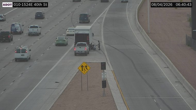 Two people attending to a trailer hitched to a pickup truck on the right shoulder