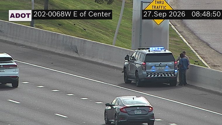 State Trooper vehicle with blue lights on the right shoulder with two individuals standing nearby