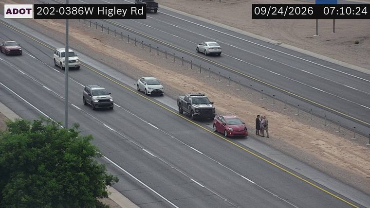 Three people standing on the right shoulder next to a red car and a pickup truck