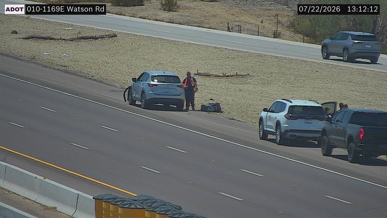 Person in high-visibility vest standing next to a vehicle on the right shoulder