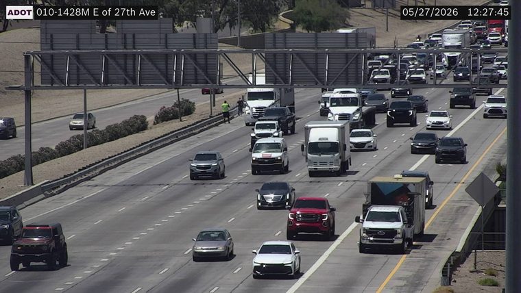 Person in a high-visibility vest walking on the left shoulder next to the median guardrail