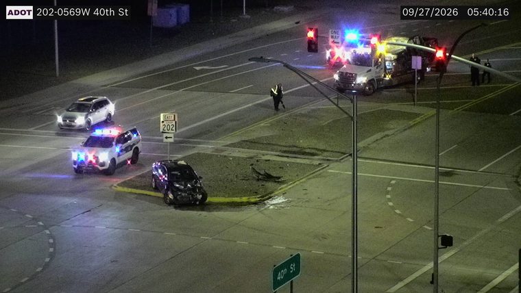 Damaged black car in the intersection, police car with lights on, and a tow truck with lights on