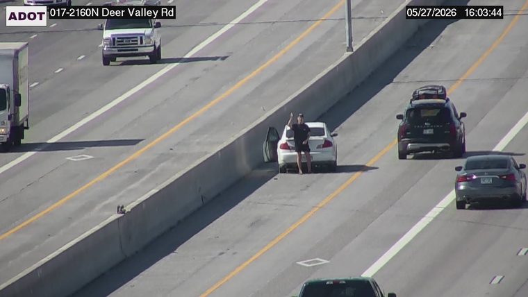 White sedan on the left shoulder with driver's door open and a person standing behind it waving