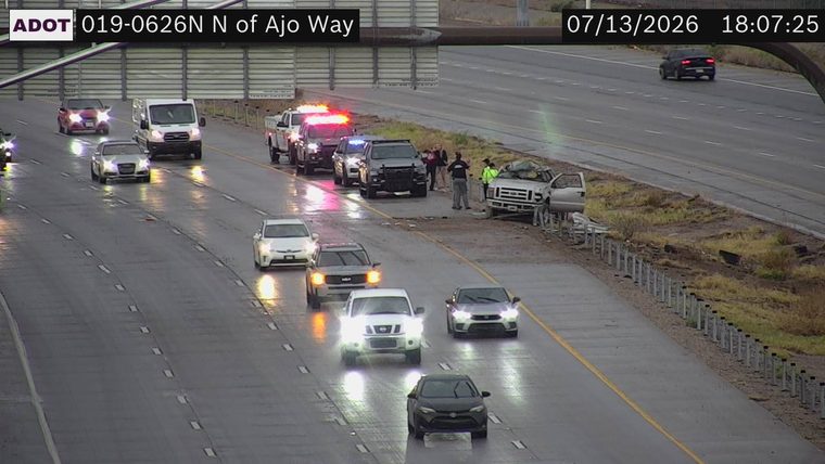 Silver pickup truck with visible collision damage on the right shoulder, multiple police vehicles with red and blue lights activated