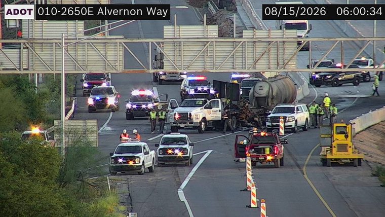 Multiple police vehicles with red and blue lights activated, a damaged tanker truck, and debris in the roadway