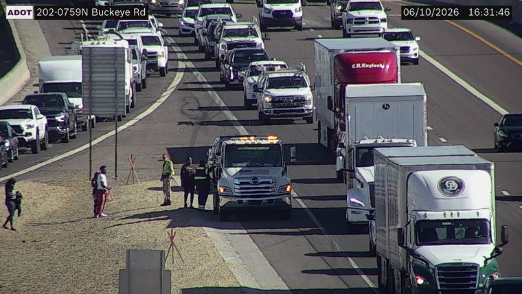 Tow truck with hazard lights on and two individuals standing next to it on the shoulder