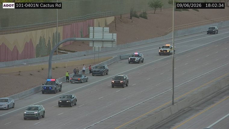 Police car with red and blue lights on the left shoulder, near a damaged silver convertible