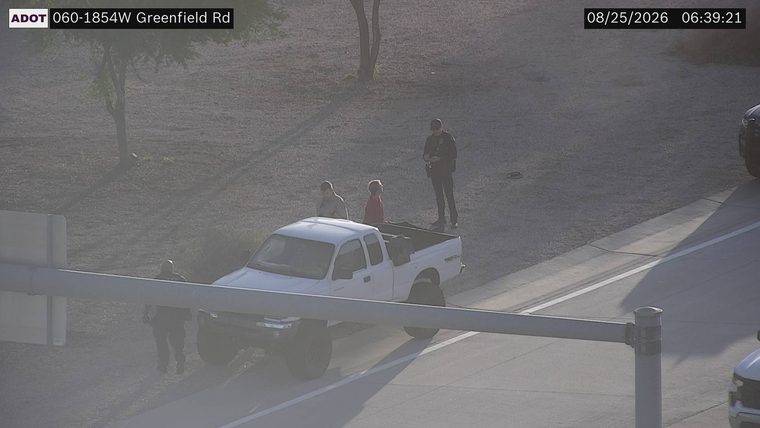 Police officer interacting with individuals next to a white pickup truck on the shoulder