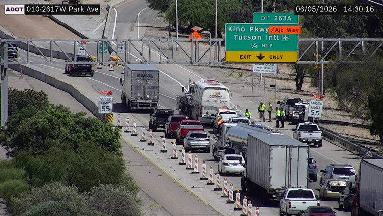 Multiple police cars and a tow truck with cones and workers in the roadway