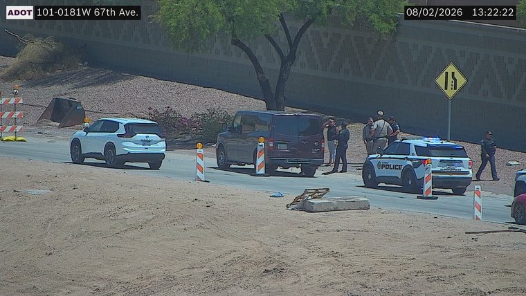 Police car with blue and red lights on the right side of the roadway, with several individuals standing nearby.