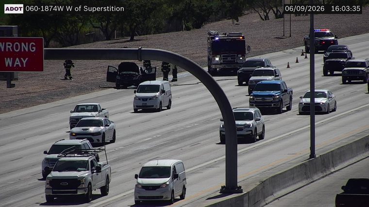 Fire truck and police car with lights on, cones, and people in uniform near a damaged vehicle in the left lanes