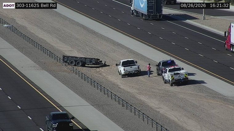 Police vehicle with blue lights on the shoulder next to a white pickup truck and a trailer
