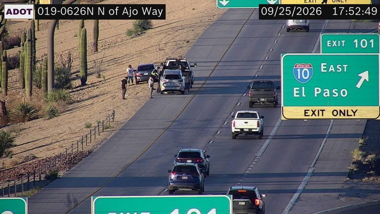 Tow truck assisting a car on the right shoulder with people standing nearby