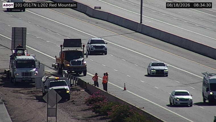 Two workers in high-visibility vests near construction equipment on the right shoulder