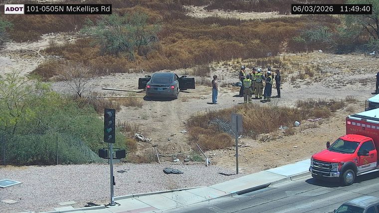 Multiple responders and an ambulance near a car with doors open off the roadway