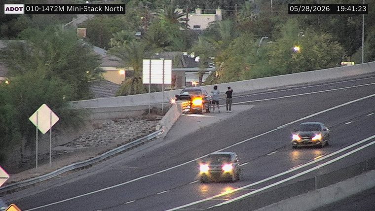 Car on the right shoulder with hazard lights on and two people standing nearby