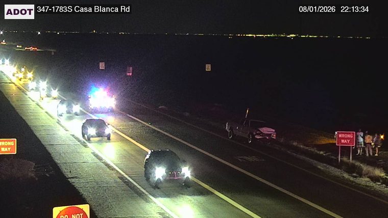 Police car with flashing lights and a damaged vehicle on the right shoulder, with several people standing nearby.
