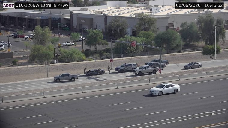 Two police cars and two civilians near a damaged car in the left lane