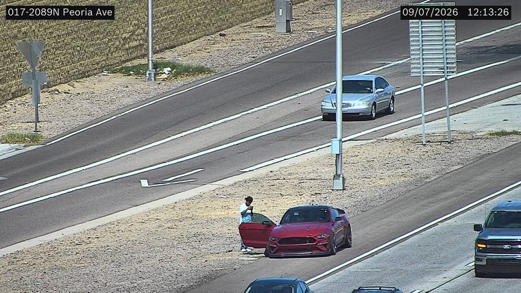 Person standing next to a red car with the driver's door open on the right shoulder