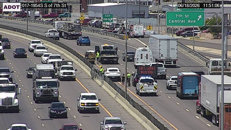 Police car with lights on the shoulder and a 'LEFT LANES BLOCKED' sign