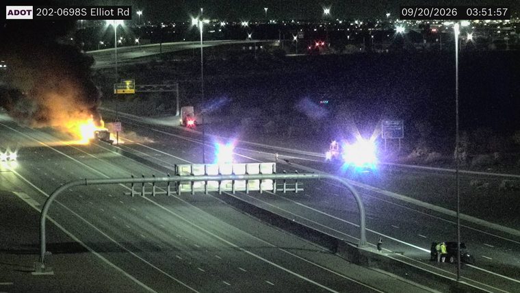 Vehicle fire in the left lanes with smoke and flames, and emergency vehicles with blue lights present