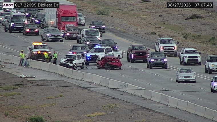 Two vehicles collided in the roadway, with one vehicle appearing to have significant front-end damage and the other rear-end damage. A police vehicle with blue lights is present, along with other emergency personnel.