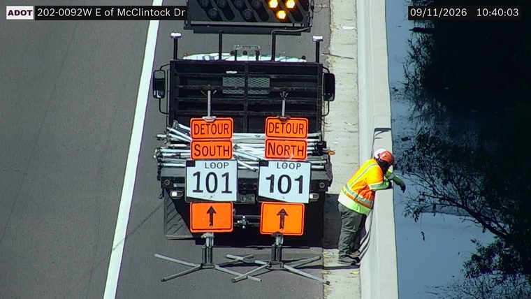 Worker in high-visibility vest and hard hat near a truck with detour signs