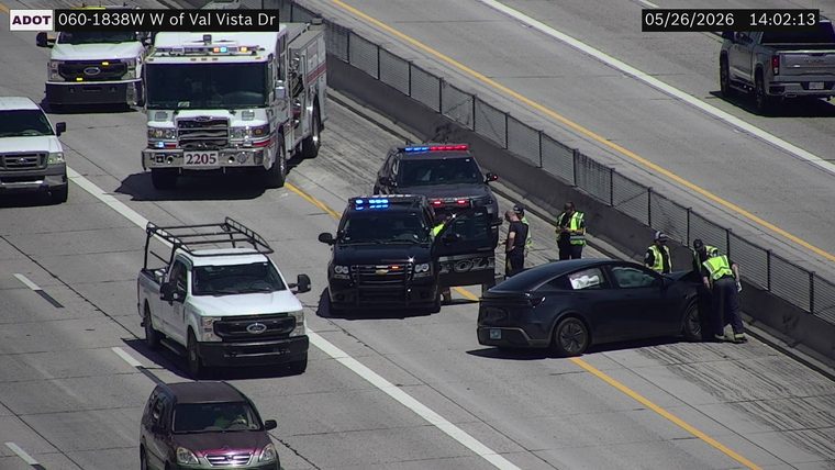 A black sedan angled against the right barrier with police vehicles, a fire truck, and emergency responders present on the right shoulder and lanes