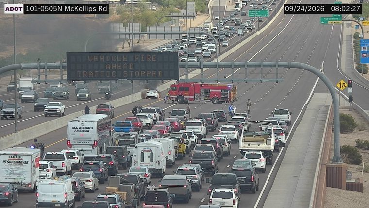 Fire and smoke from a white car in the left lanes, with a fire truck and responders present