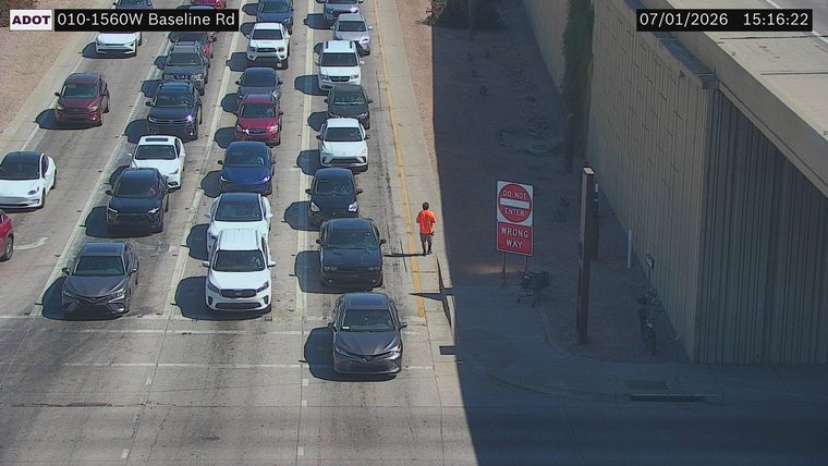 Person in orange shirt walking on the side of the road near a "Do Not Enter Wrong Way" sign