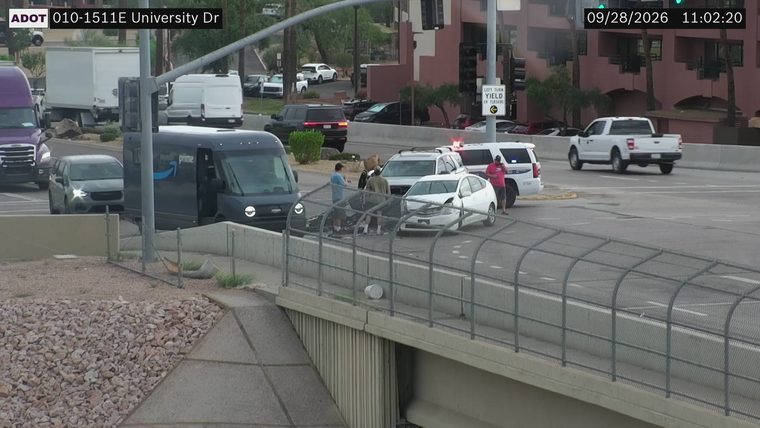 White sedan with visible front-end damage and a police SUV with lights on in the travel lanes