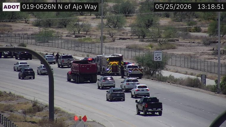 Fire truck and police vehicles with flashing lights on the roadway, with responders standing near vehicles on the left shoulder