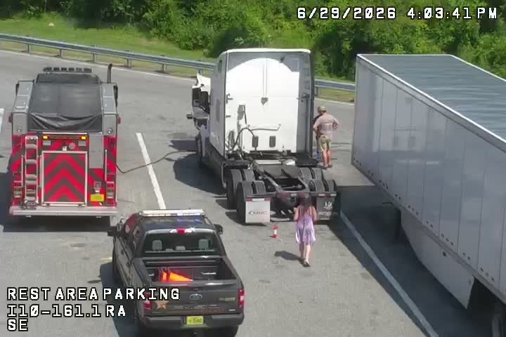 Fire truck and police vehicle present with a person standing near a semi-truck