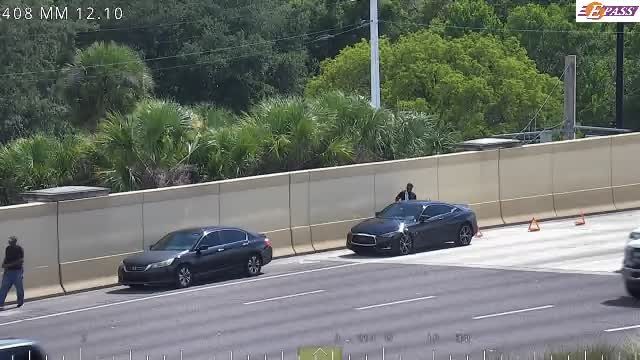Person standing by a car on the shoulder, with traffic cones present.