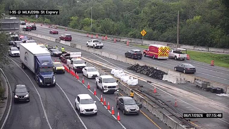Emergency vehicles and personnel on scene with traffic cones and barriers.