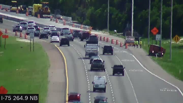 A red trailer has crashed and is on its side on the shoulder of the road.