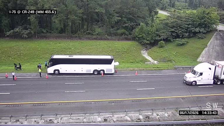Bus stopped on shoulder with people and cones, FedEx truck nearby.