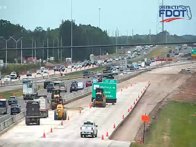 Construction vehicles and cones on the roadway, traffic is backed up.